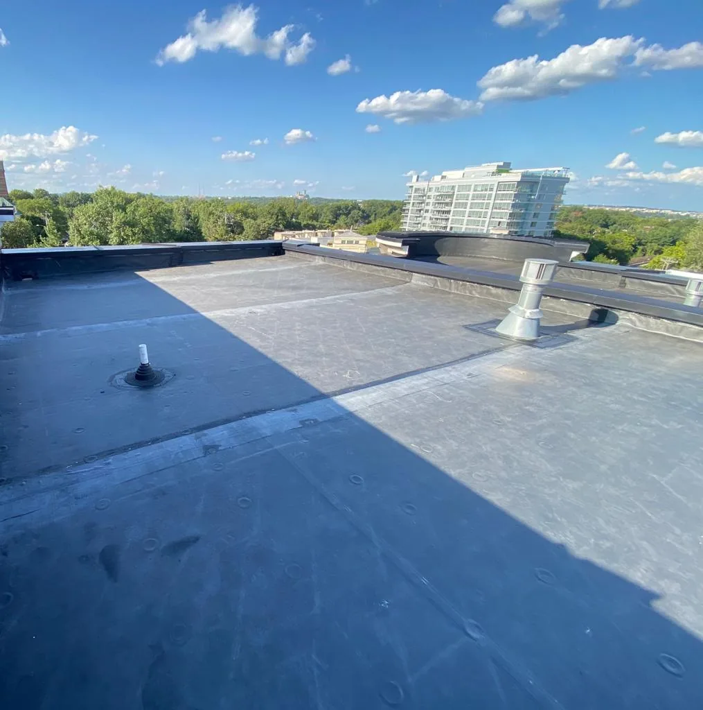 Low-slope membrane roof with pipe boots, a vent and parapet flashing on a mid-rise building